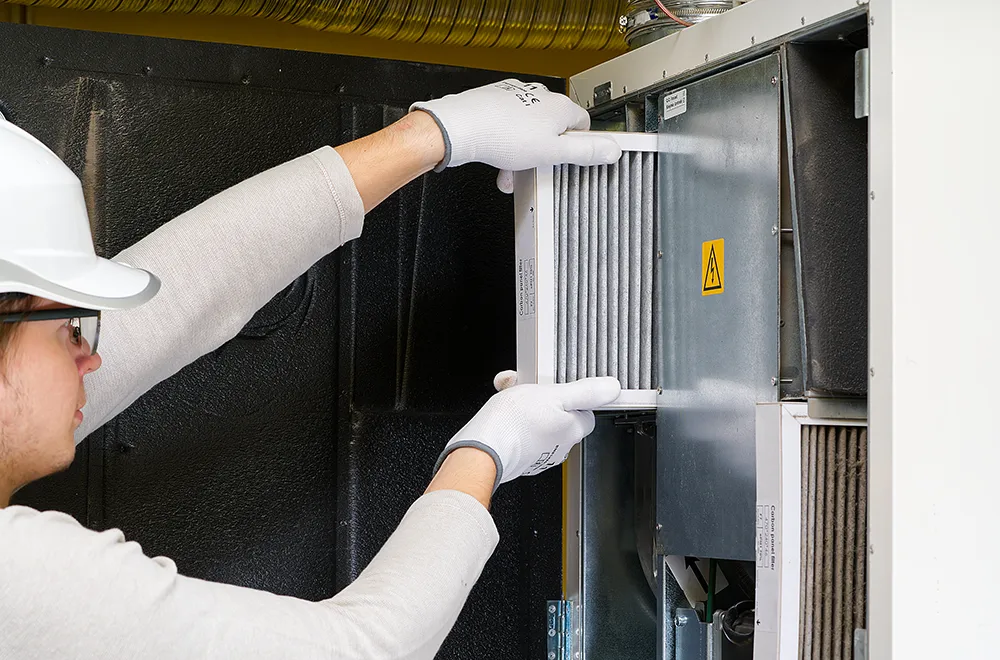a worker pulling out an hvac units filter to clean it